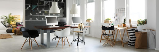 A large, bright room with four windows and contemporary furnishings. They include a large table with three computer stations.